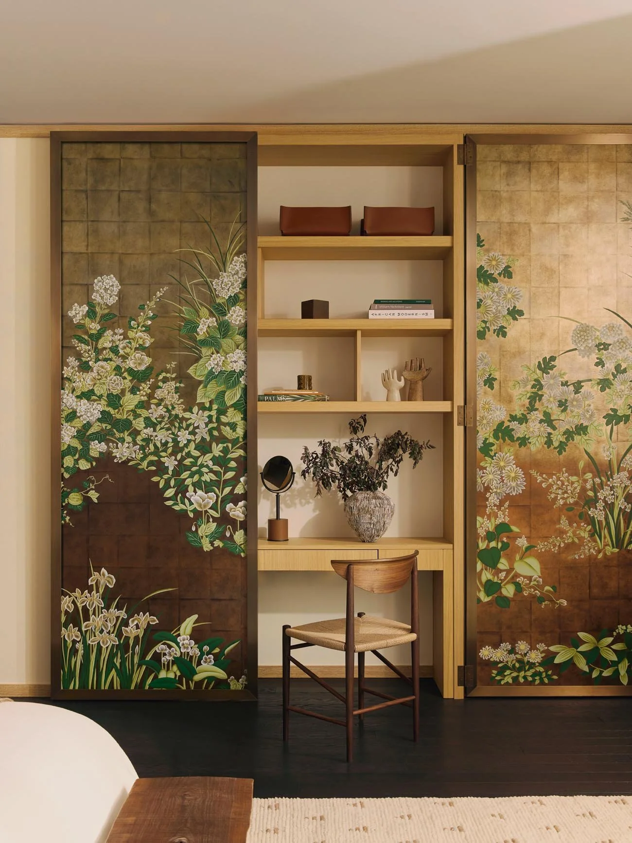 A refined interior with a hidden wooden desk and chair, alongside decorative sliding doors with De Gournay wallpaper in green, white, and gold floral patterns.
