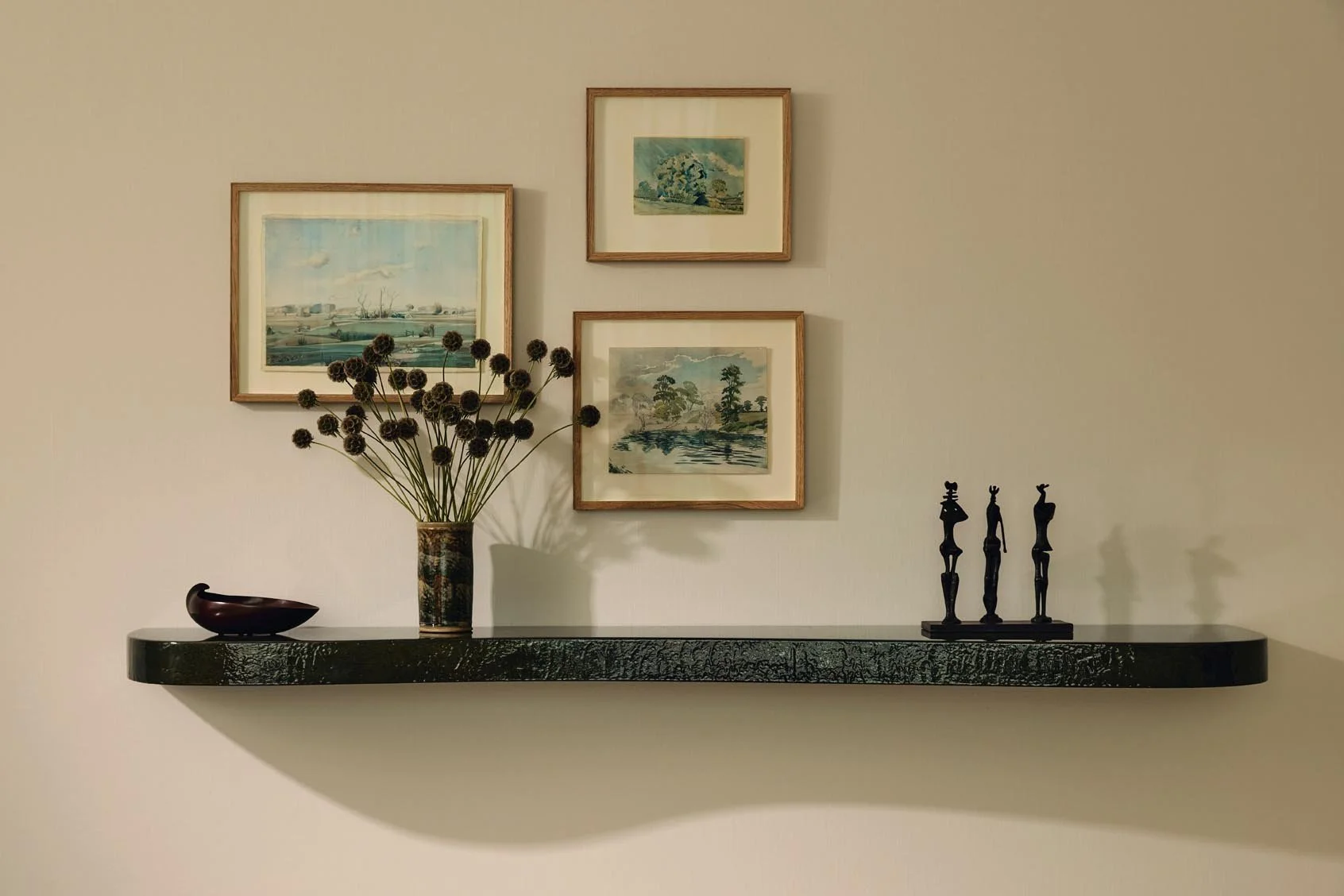 Luxury decorative wall shelf at The Peninsula Hotel Residences featuring framed artwork, a vase with dried flowers, a small wooden bowl, and a bronze sculpture.