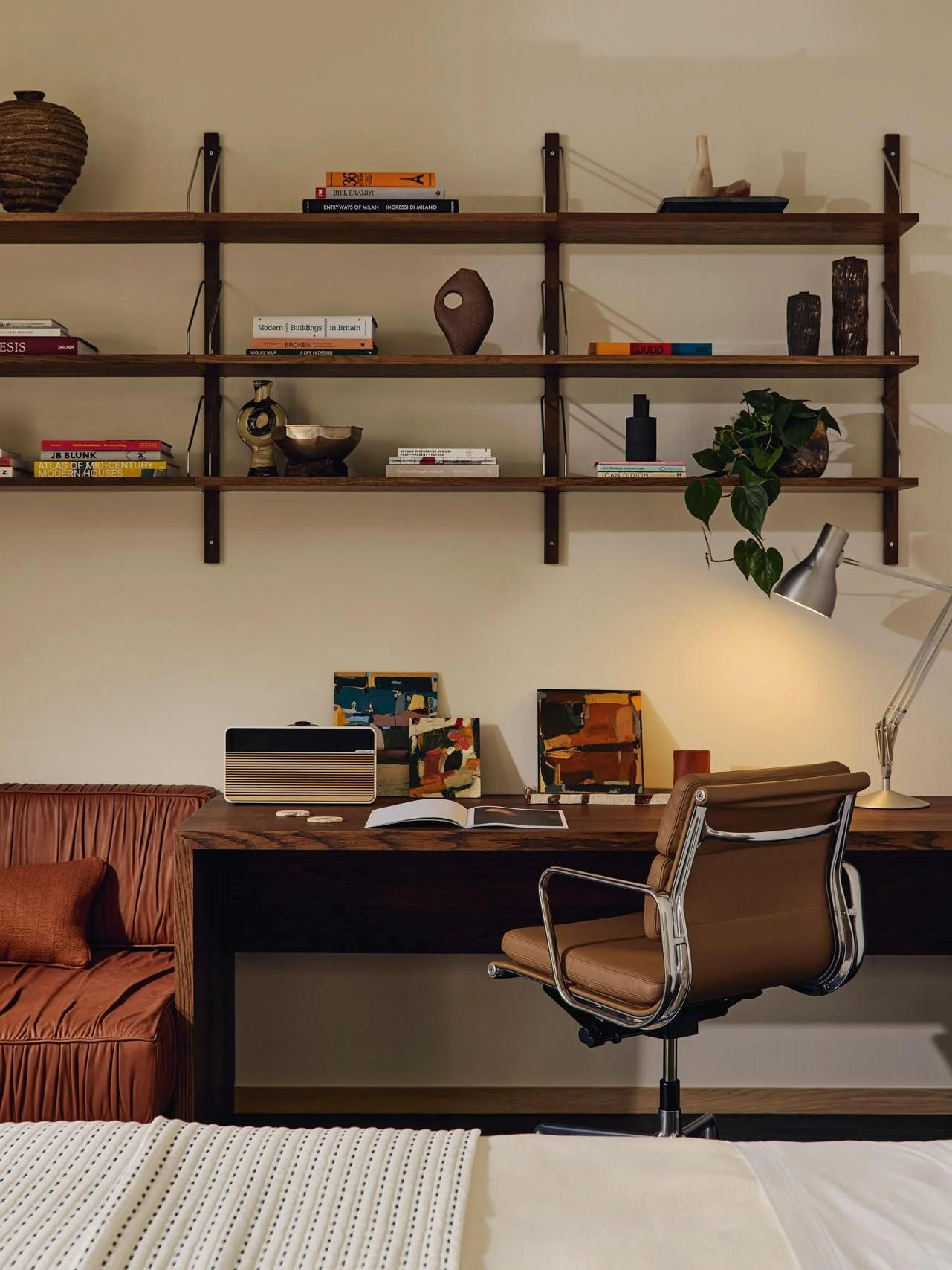 Stylish home office at The Peninsula Hotel Residences featuring a wooden desk, brown leather office chair, and Scandinavian wall-mounted shelves curated with books, decorative objets, and a plant, accented by a desk lamp and artwork.