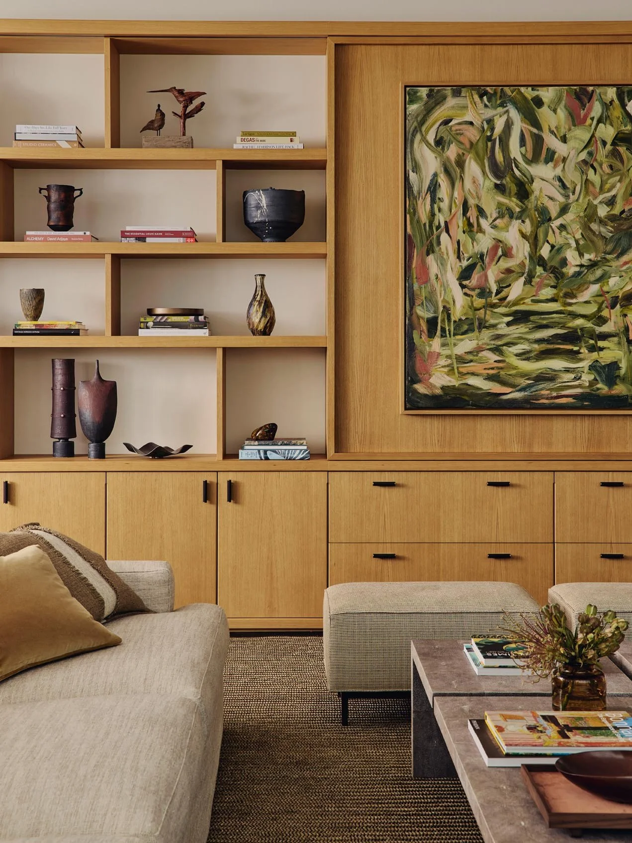 Luxury living room at The Peninsula Hotel Residences featuring a beige sofa with cushions, a shagreen coffee table, and a wooden wall unit curated with ceramics, vases, decorative objets, books, and a large abstract painting.