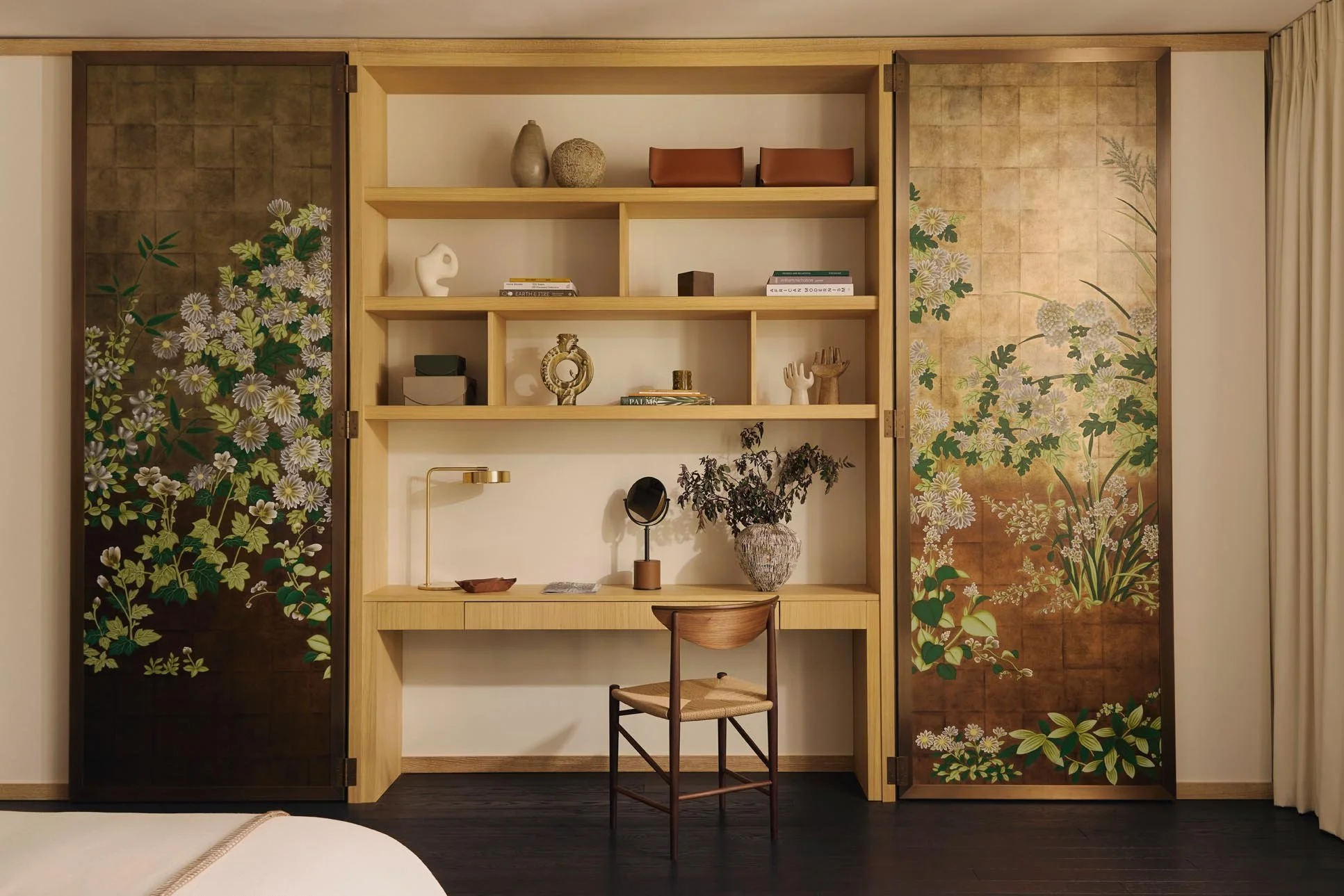 A refined interior with a hidden wooden desk and chair, alongside decorative sliding doors with De Gournay wallpaper in green, white, and gold floral patterns.