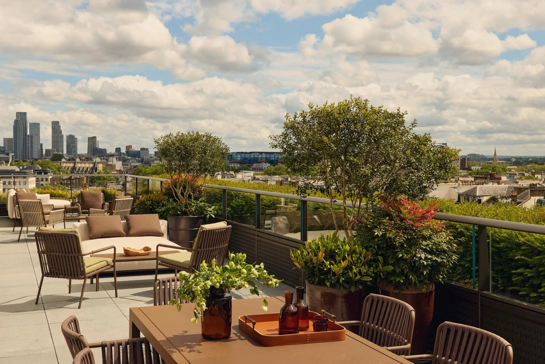 Rooftop patio at The Peninsula Hotel Residences featuring outdoor furniture and potted plants, with panoramic city skyline views of London.