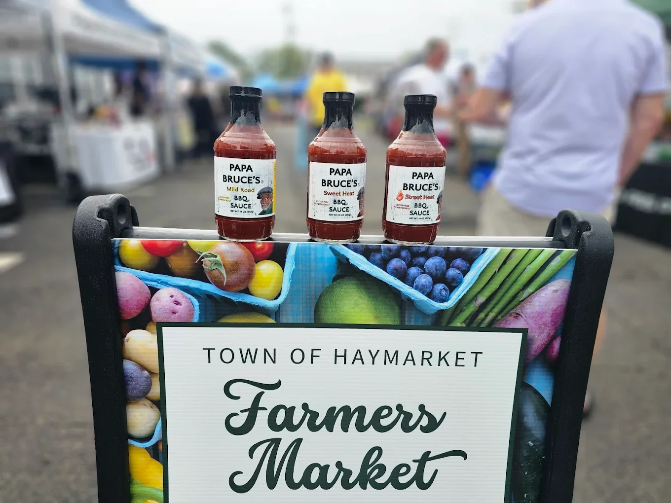 Sign at Haymarket farmers market, with blurred market stalls and people in the background.