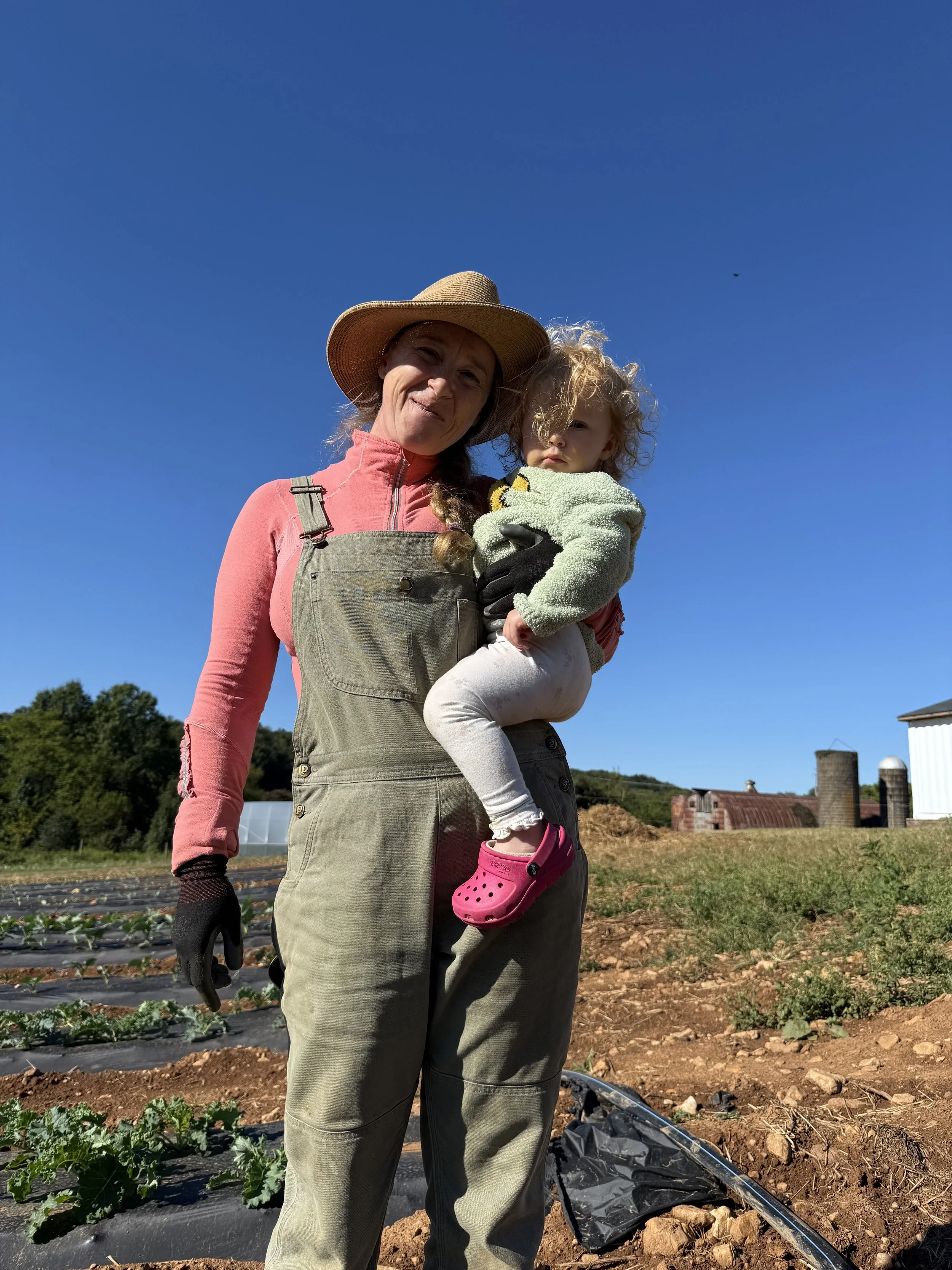 Woman holding a young girl in a farm field under a clear blue sky.