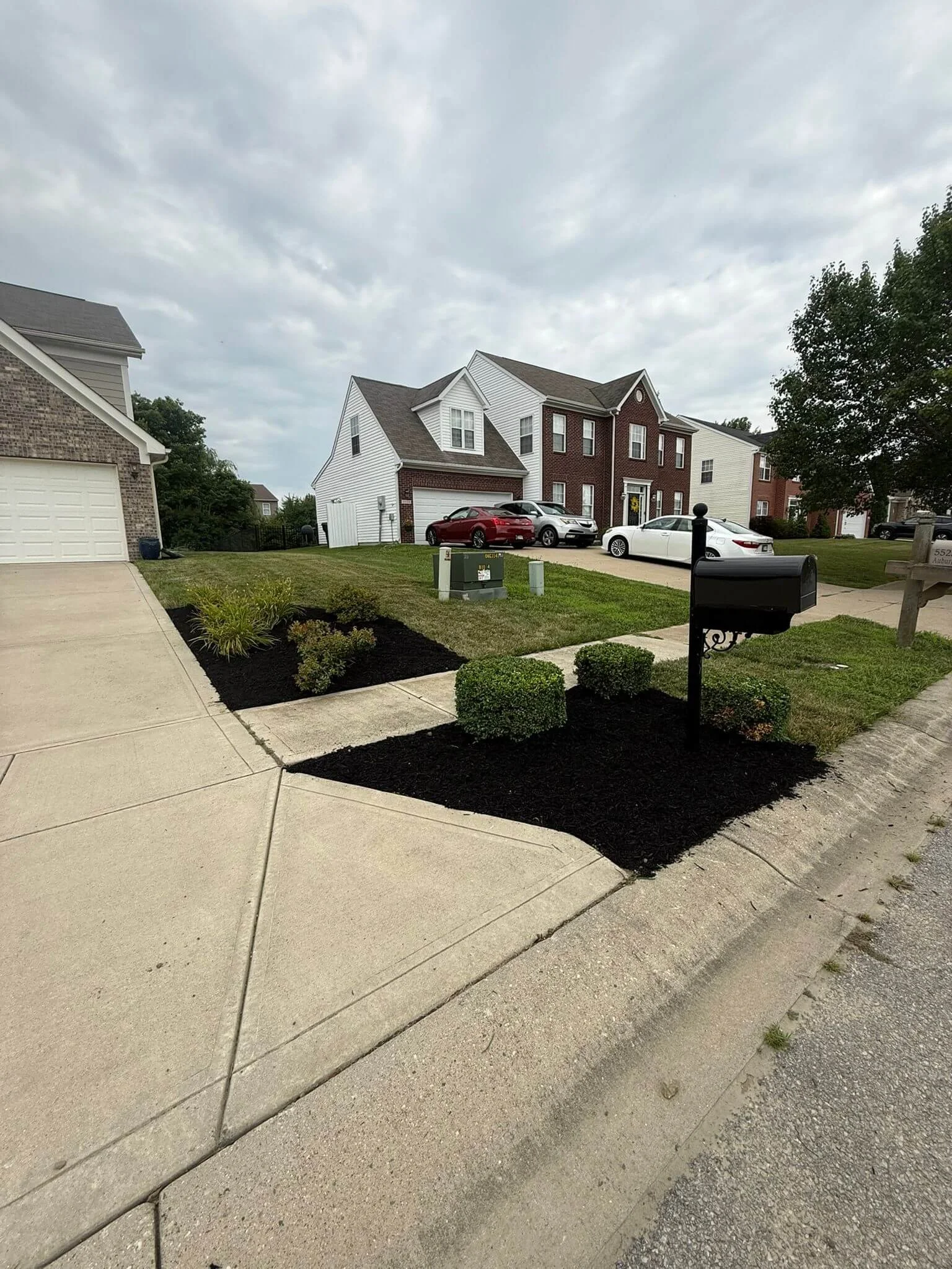 Residential neighborhood with a house, parked cars, mailbox, and freshly landscaped yard.