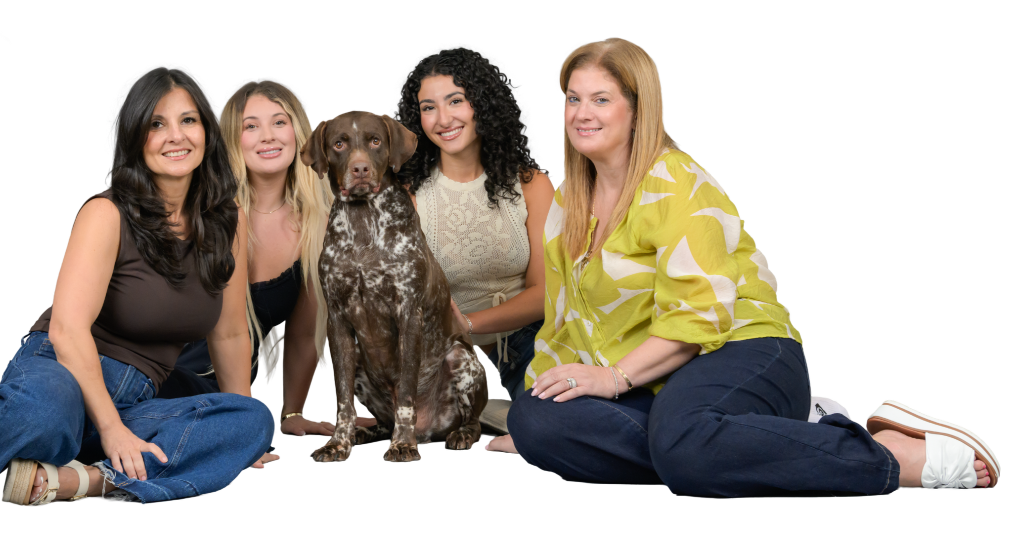 Four women and one dog sitting on the floor, smiling, with a black background.