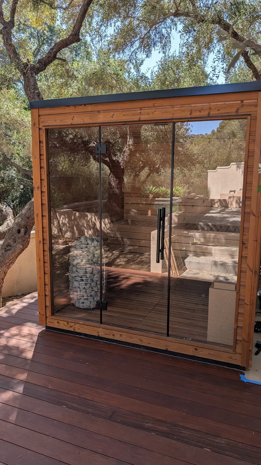 Prefab outdoor sauna assembled on a backyard deck — glass front, electric heater, ready to use.