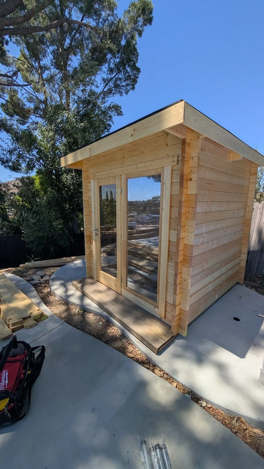 Cabin sauna assembled on a concrete pad — glass door and sidelight, interlocking timber.