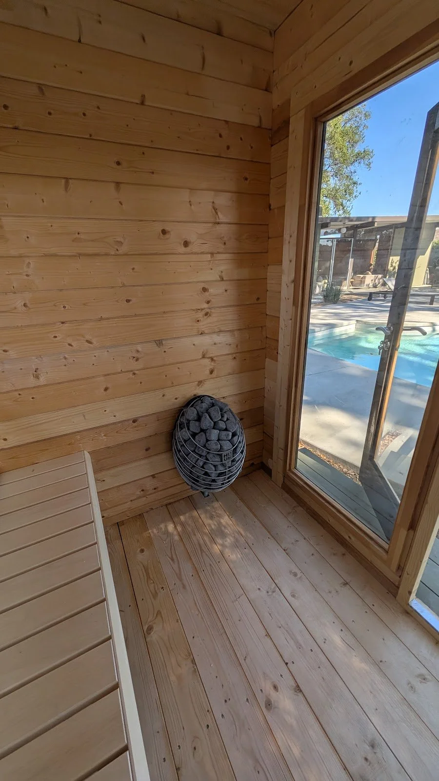 HUUM heater in, stones loaded — looking out to the pool. Prefab kit, owner-installed.