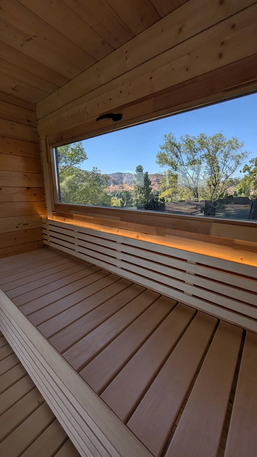 Cabin sauna interior after assembly — panoramic window, LED backrest lighting.