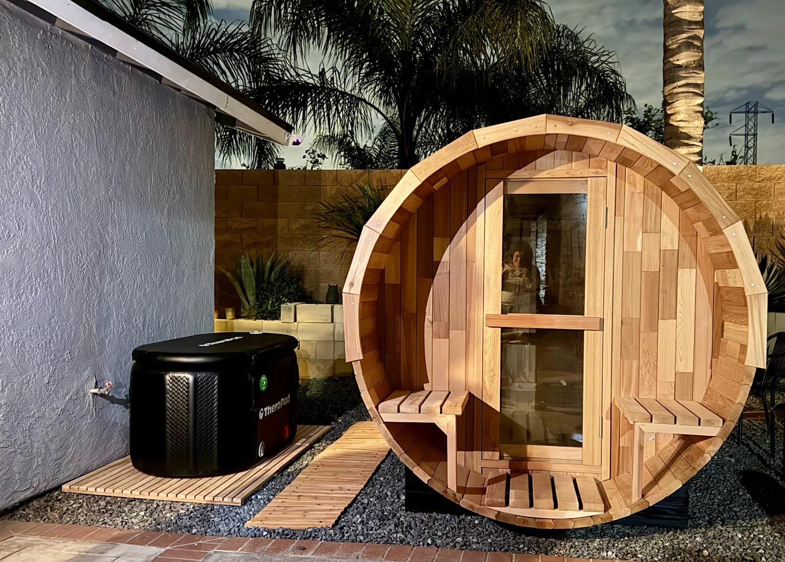 Barrel sauna with porch seating — assembled and leveled on a prepared pad.