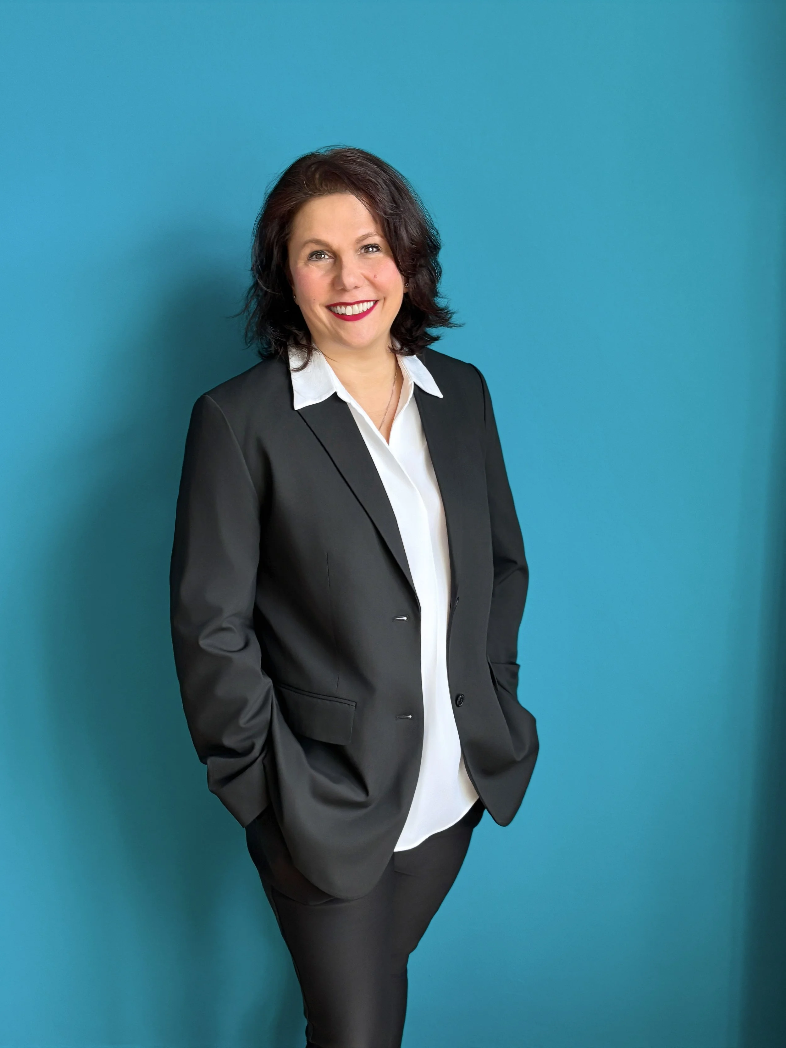 Eine smiling Frau in formeller schwarzer Anzug vor einem blauen Hintergrund.