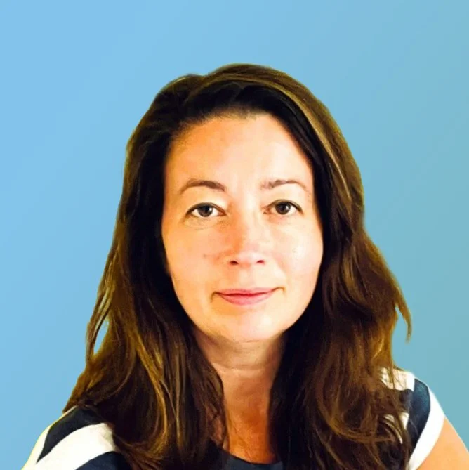 A woman with long brown hair and light skin, wearing a striped shirt, facing the camera with a neutral background.