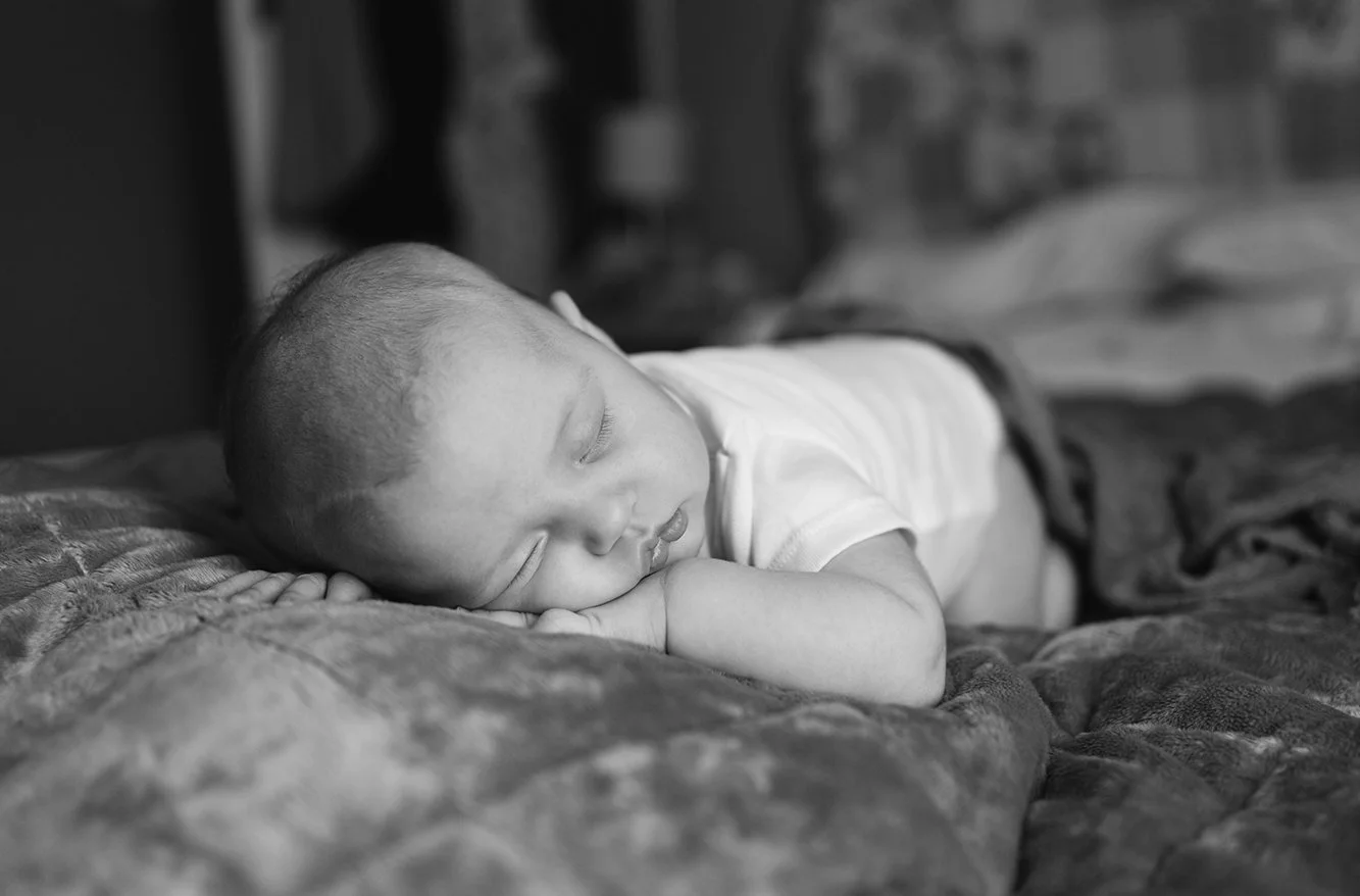 Newborn photographer Bristol - black and white image of a baby sleeping on a bed during a baby photoshoot at home in Bristol..