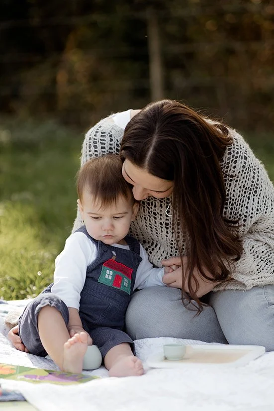 Family photographer gloucestershire - Mother holding her little boy's hand while sitting on the grass.