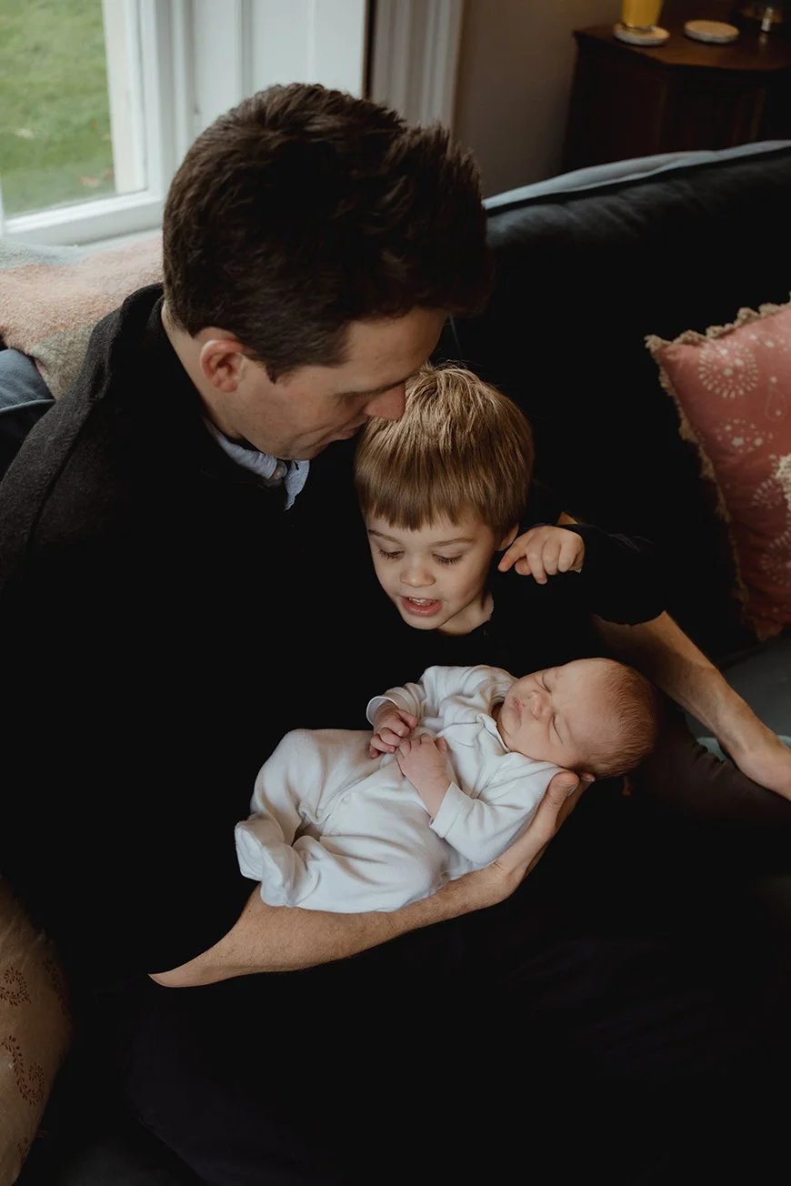 Newborn and family photographer Bath - image of a father and brother looking at baby.