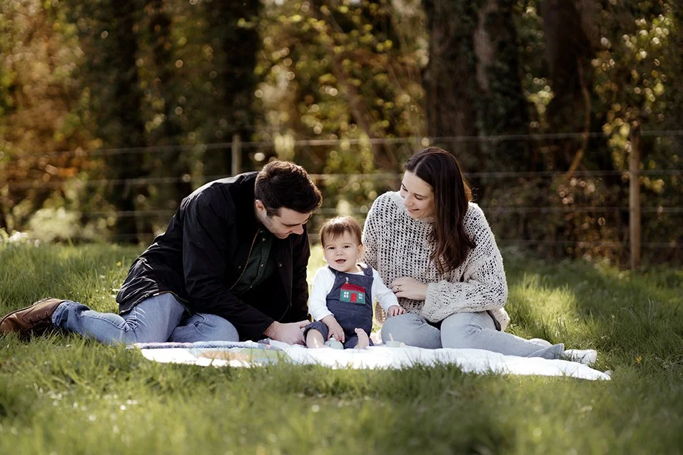 Family photographer gloucestershire - Parents with their one year old sitting on the grass.