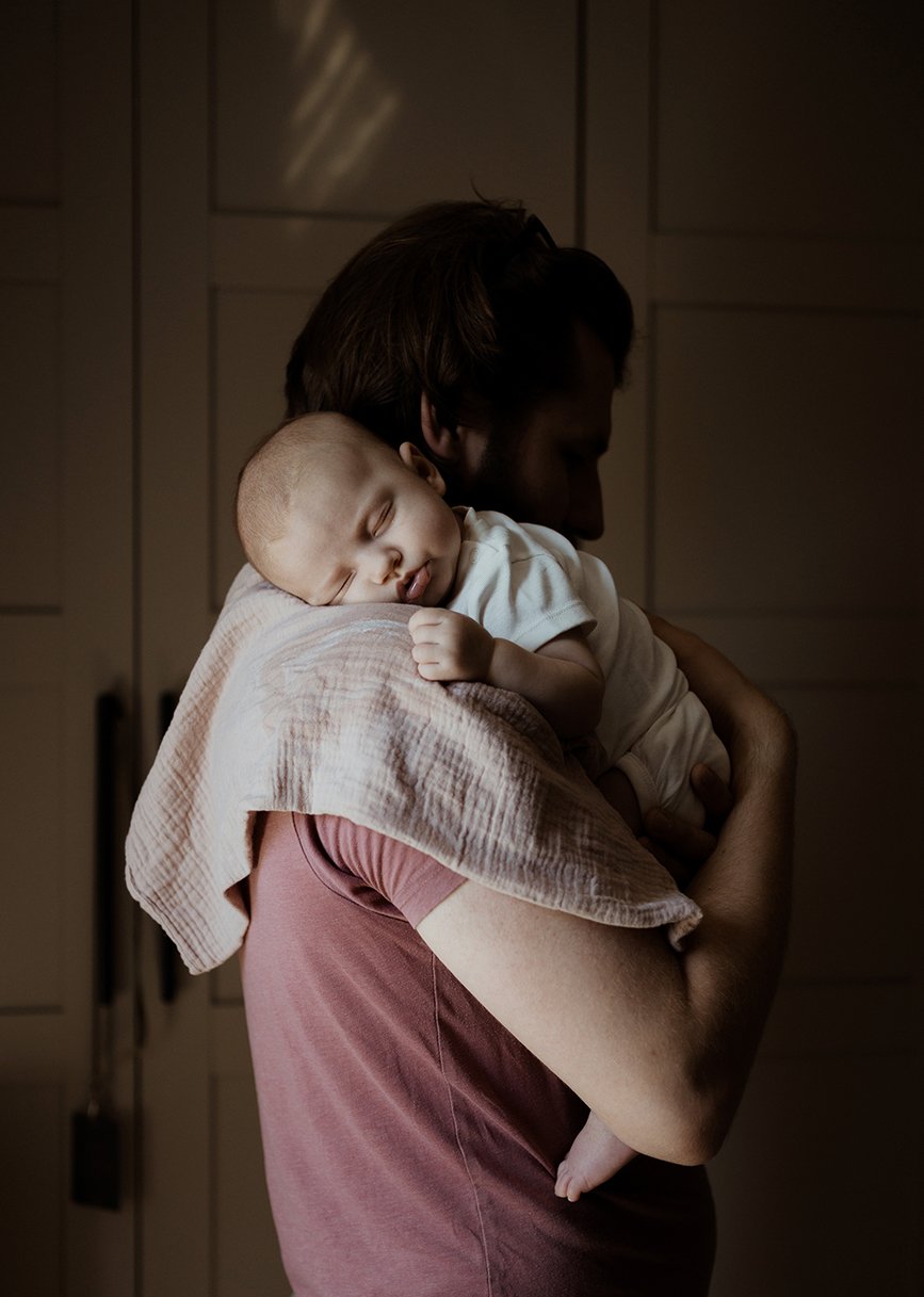 Newborn photographer Bristol - image of a father holding his baby who is sleeping on his shoulder.