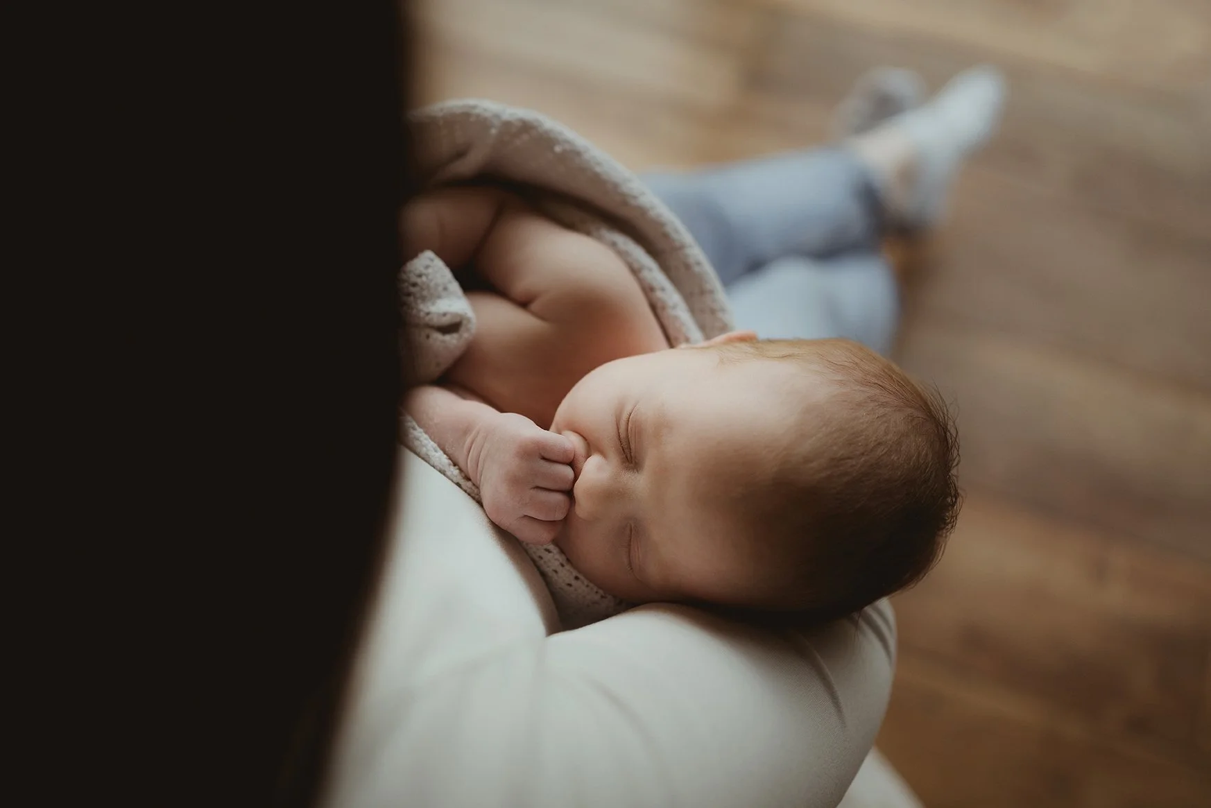 Newborn baby sleeping in their mother’s arms, in soft natural light.