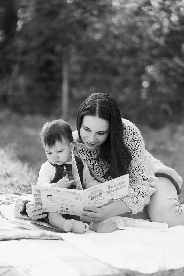 Black and white picture of a mother reading a book to her little boy while sitting on the grass.
