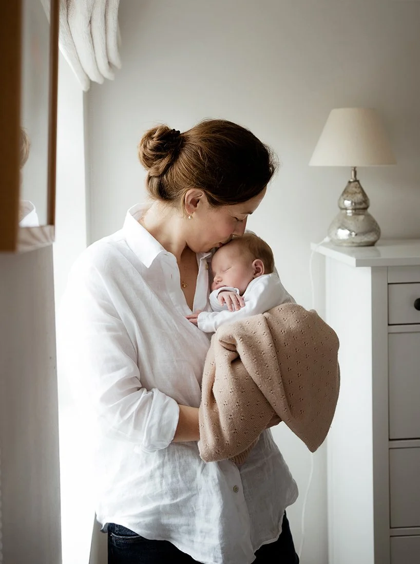 Image of a mother kissing the top of her baby's head during a newborn photoshoot in their home in Bath.