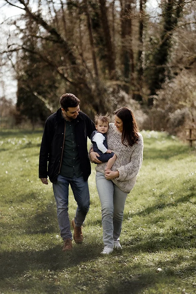Parents with their one year old boy walking along in a field during a photoshoot.