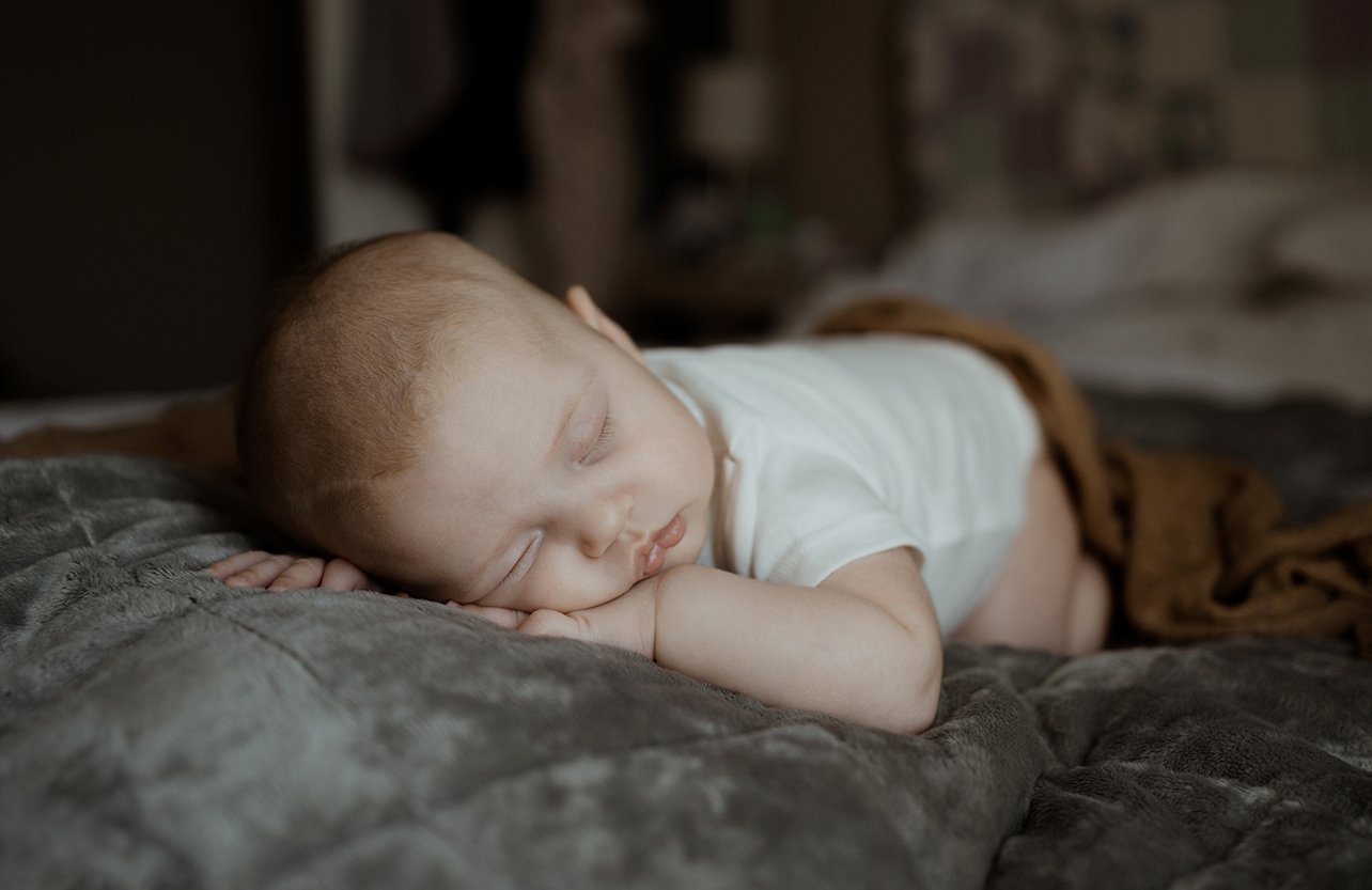 Newborn photographer Bristol - image of a baby sleeping on a bed during a baby photoshoot at home in Bristol.