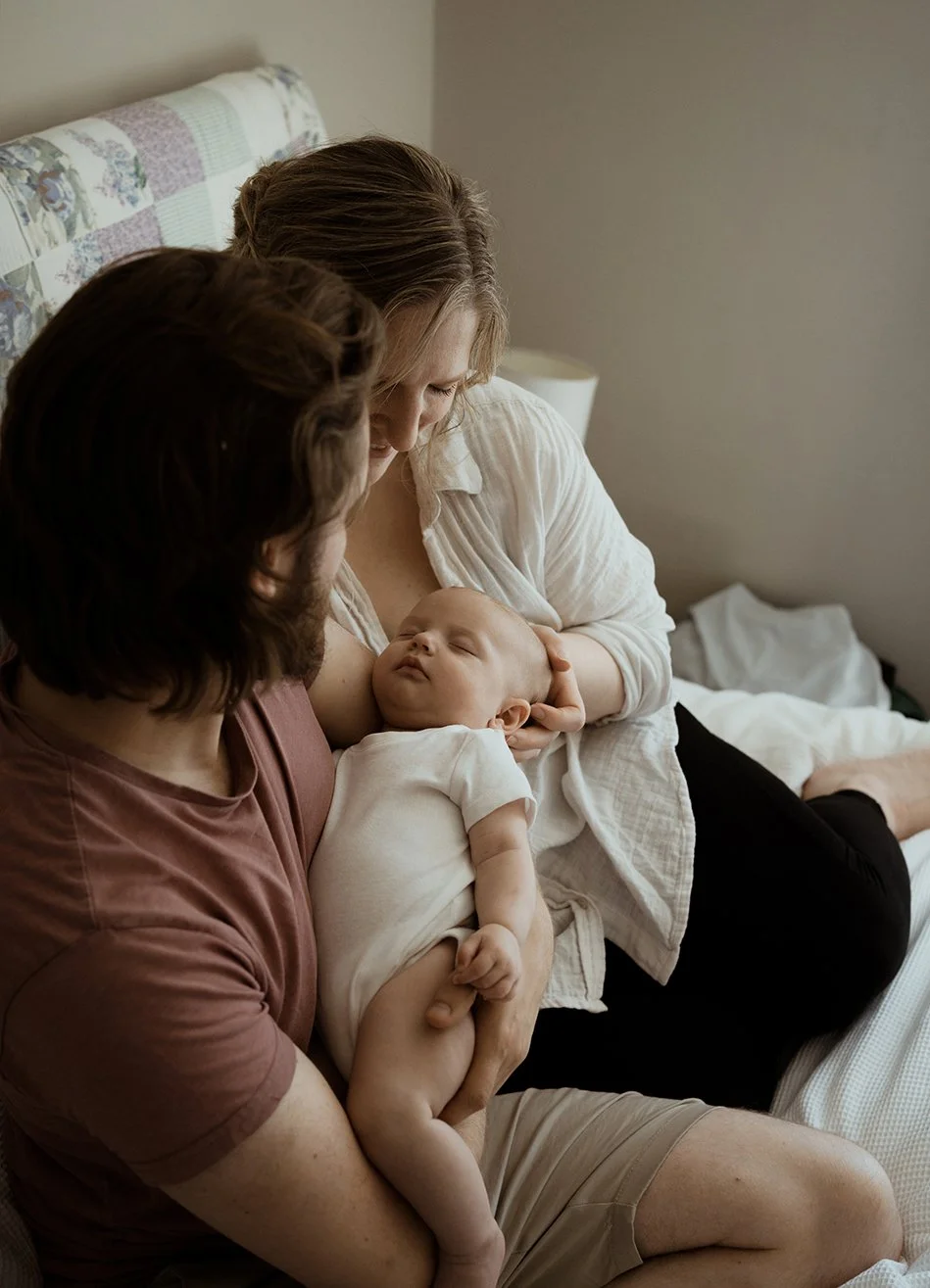 Newborn photographer Bristol - image of a couple with their newborn baby sitting on their bed during a baby photoshoot at their home in Bristol.