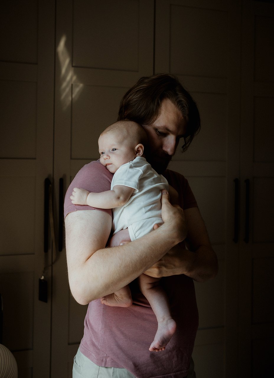 Newborn photographer Bristol - image of a father holding his baby who is looking out of a window.