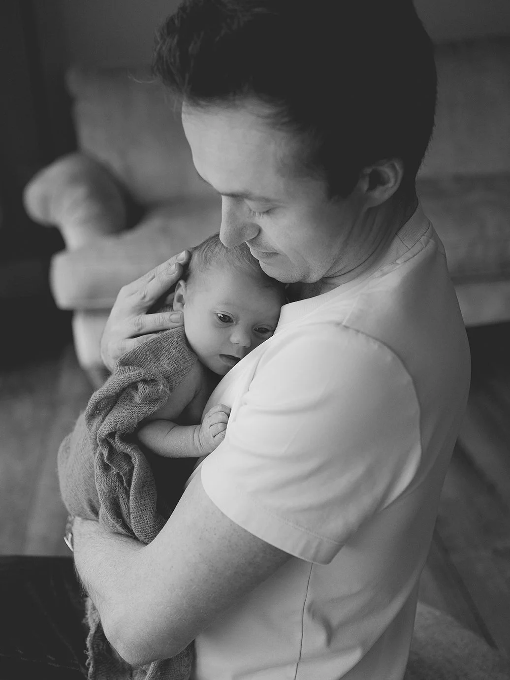 Black and white image of father holding newborn baby during a newborn photoshoot.