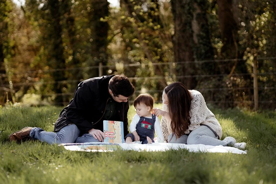 Family photographer gloucestershire - Parents with their one year old sitting on the grass.