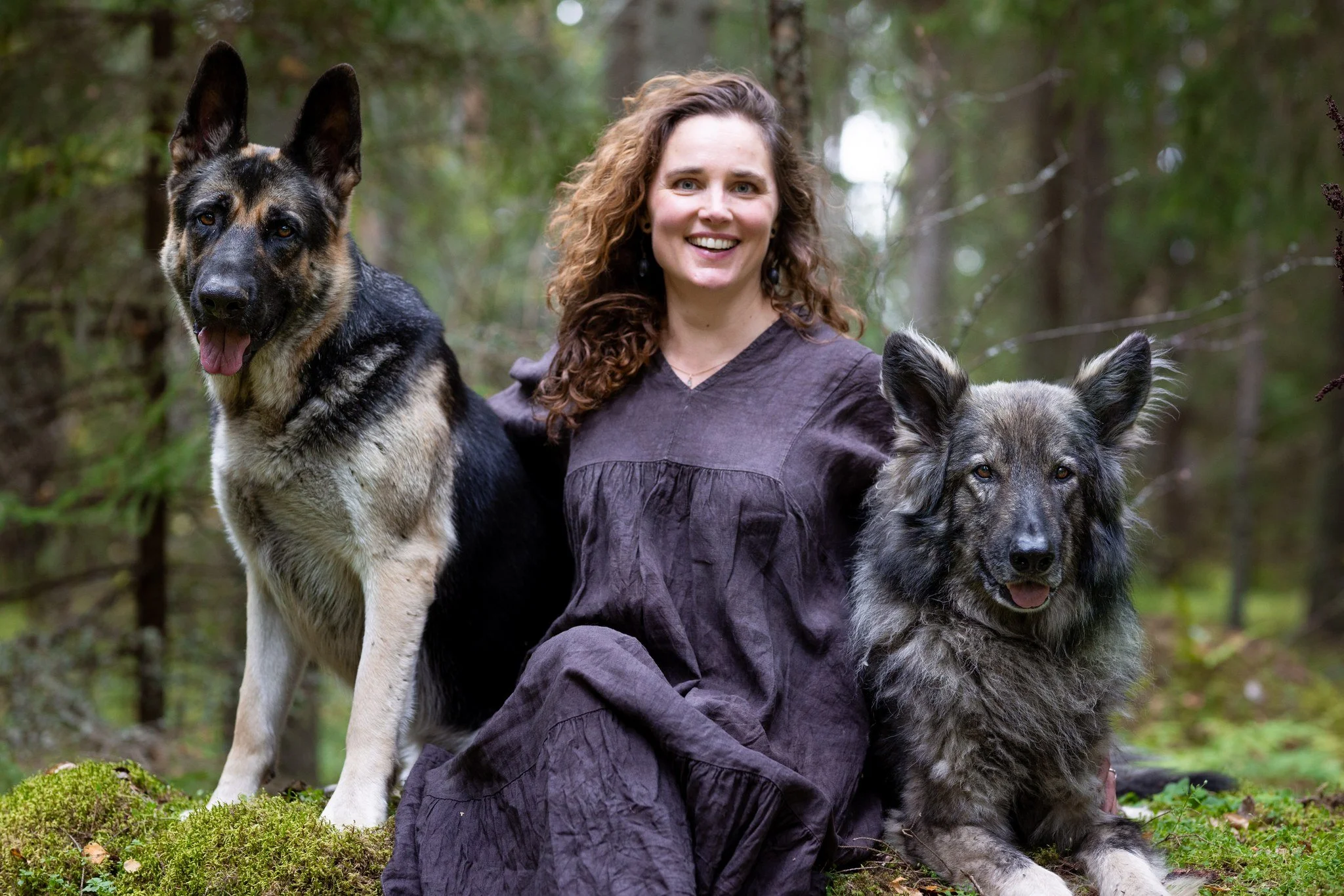 Henriika istuu kivellä metsässä kahden koiransa kanssa.