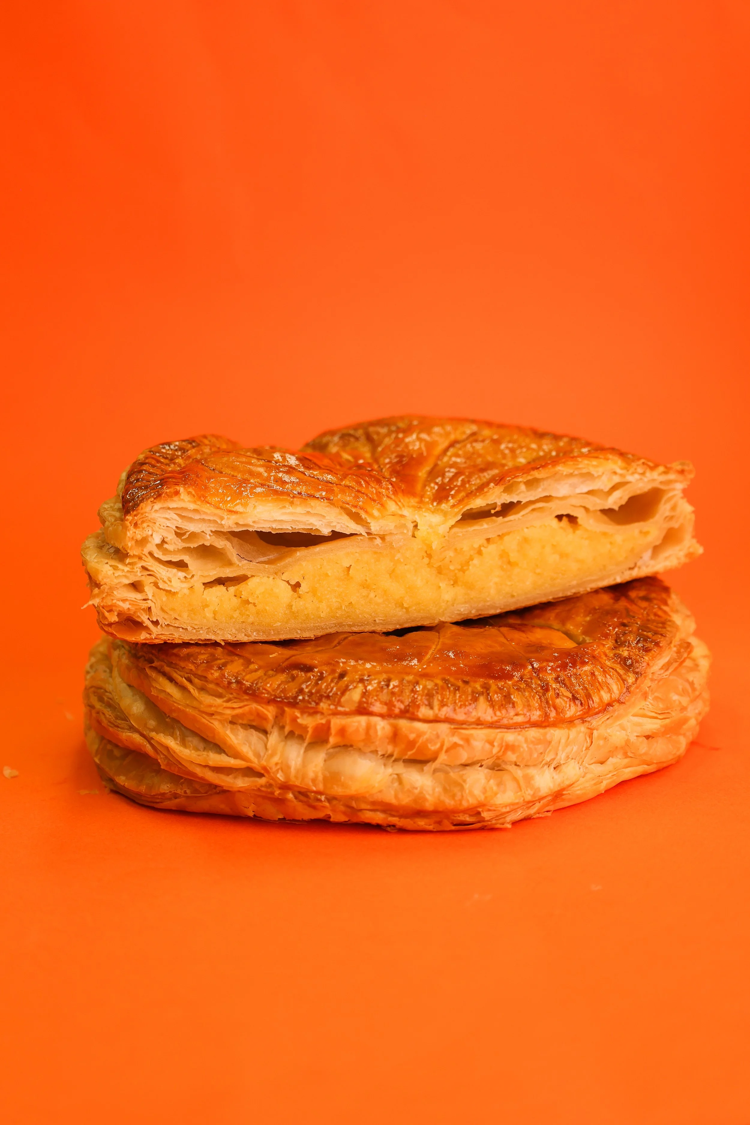 Close-up of a flaky, golden pastry with a filling, on an orange background.