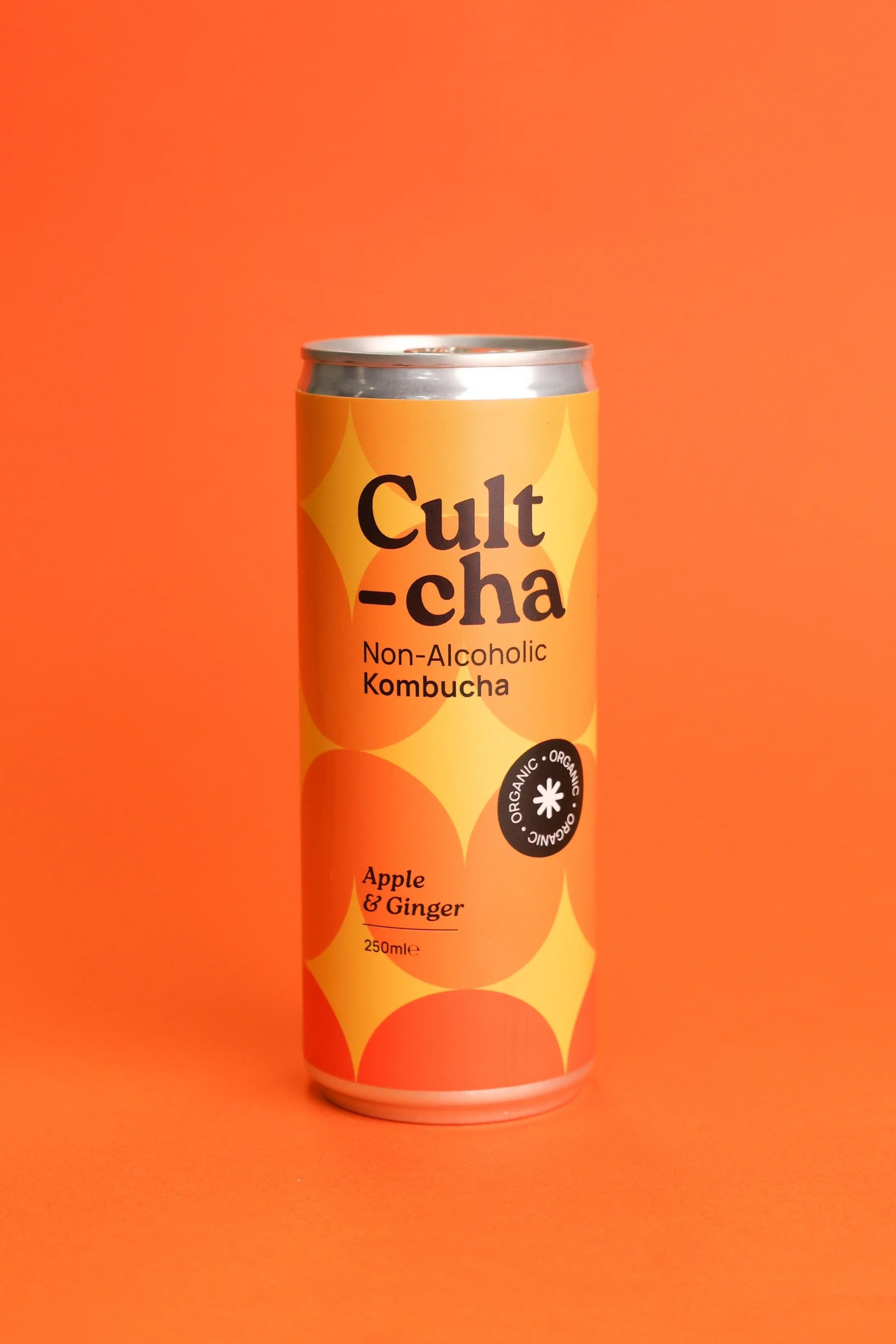 A can of Cult-cha non-alcoholic kombucha with apple and ginger flavor, set against an orange background.