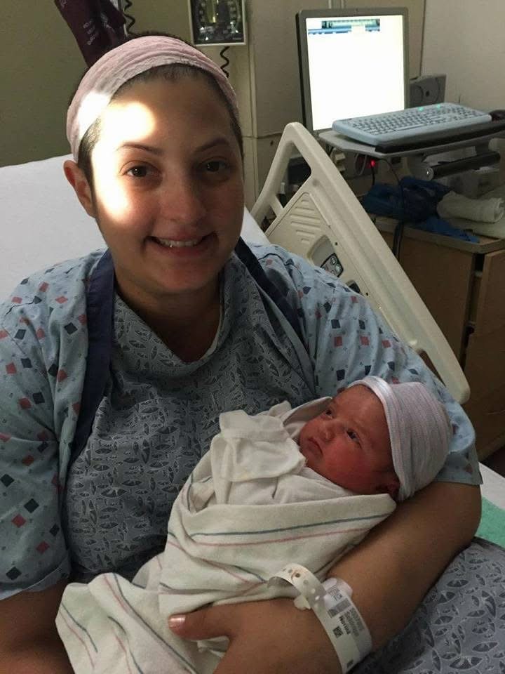 A woman in a hospital bed holding a newborn baby wrapped in a blanket, both wearing hospital attire.