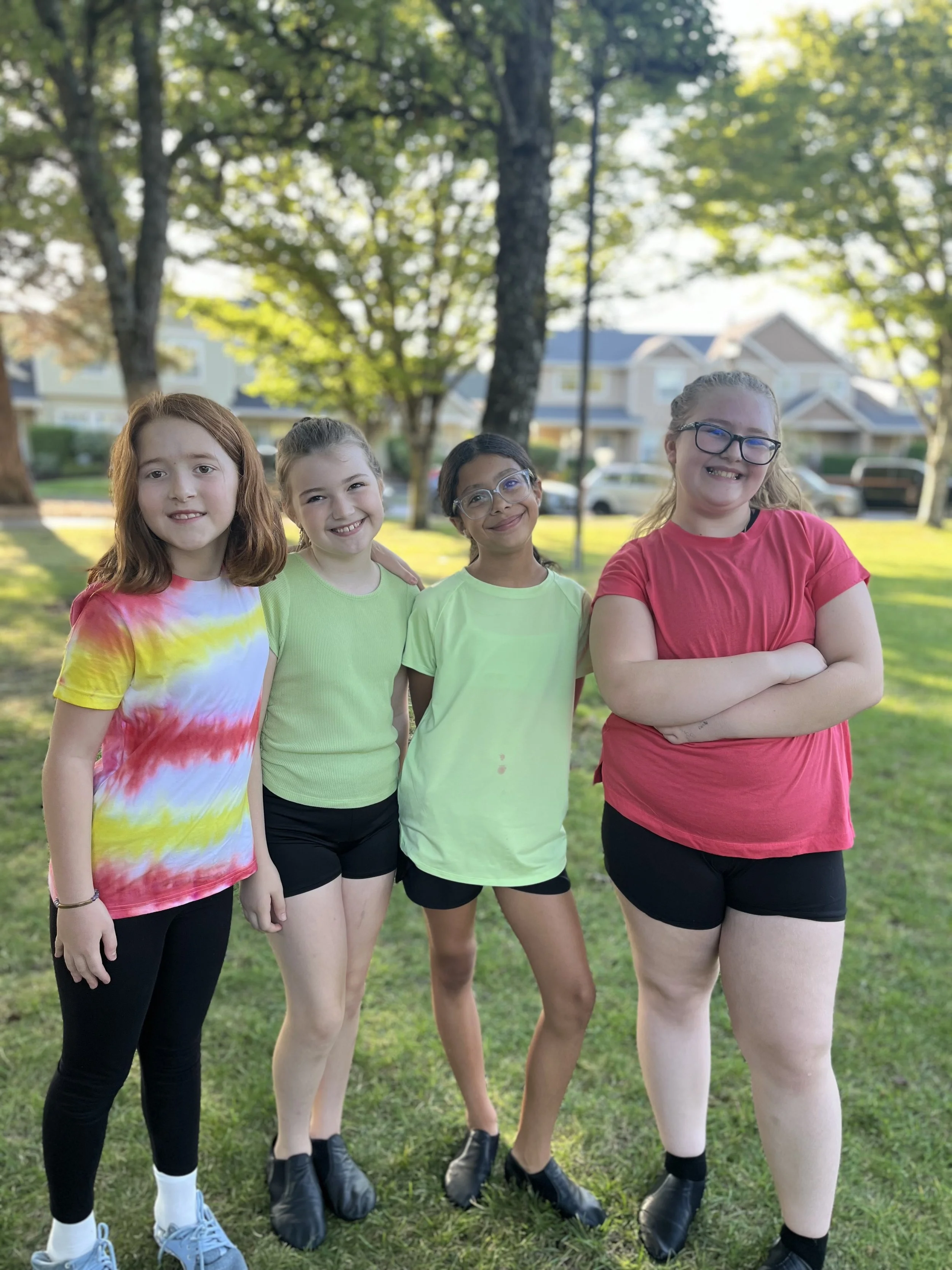 Four girls smiling and standing together on a grassy field at a park at the 2024 HID Summer Showcase.