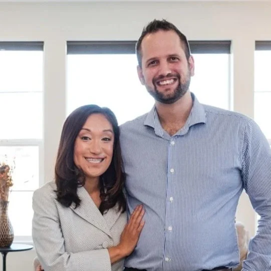 Melissa & Chris are a Six Leaf Design clients and owners of Power Up Software. Their photo shows a smiling woman and man standing together indoors in front of windows, with the woman resting her hand on the man's chest.