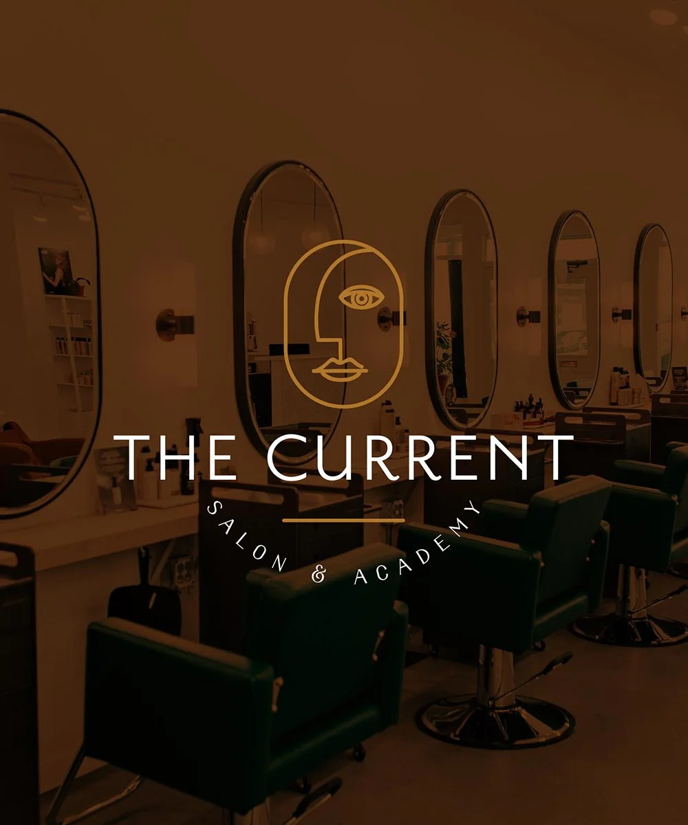 A modern hair salon logo design overlaid on an image of the salon with green chairs and mirror stations, illuminated with warm lighting, branded as 'The Current Salon & Academy'