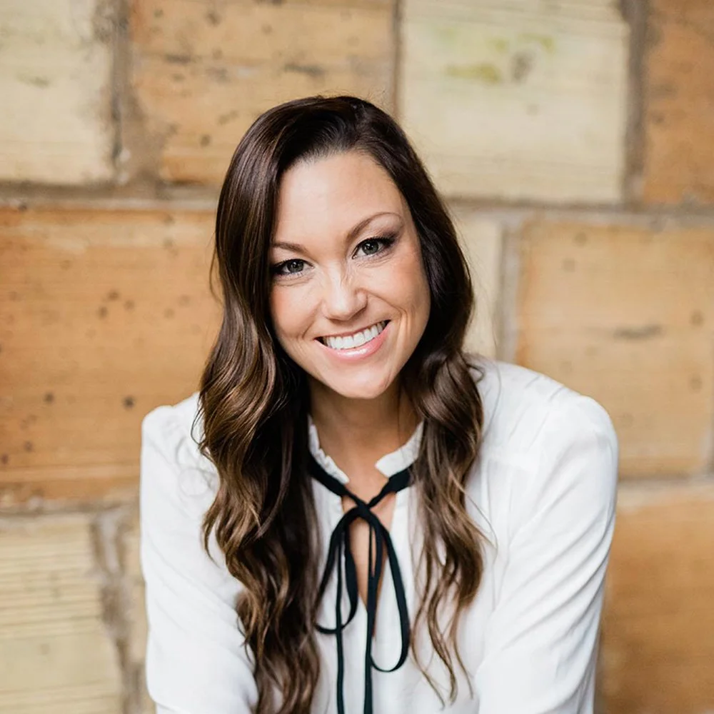 Emmie Schulte is a Six Leaf Design client and owner of Schulte Consulting Services. She is a woman with long brown wavy hair smiling in front of a wooden wall.