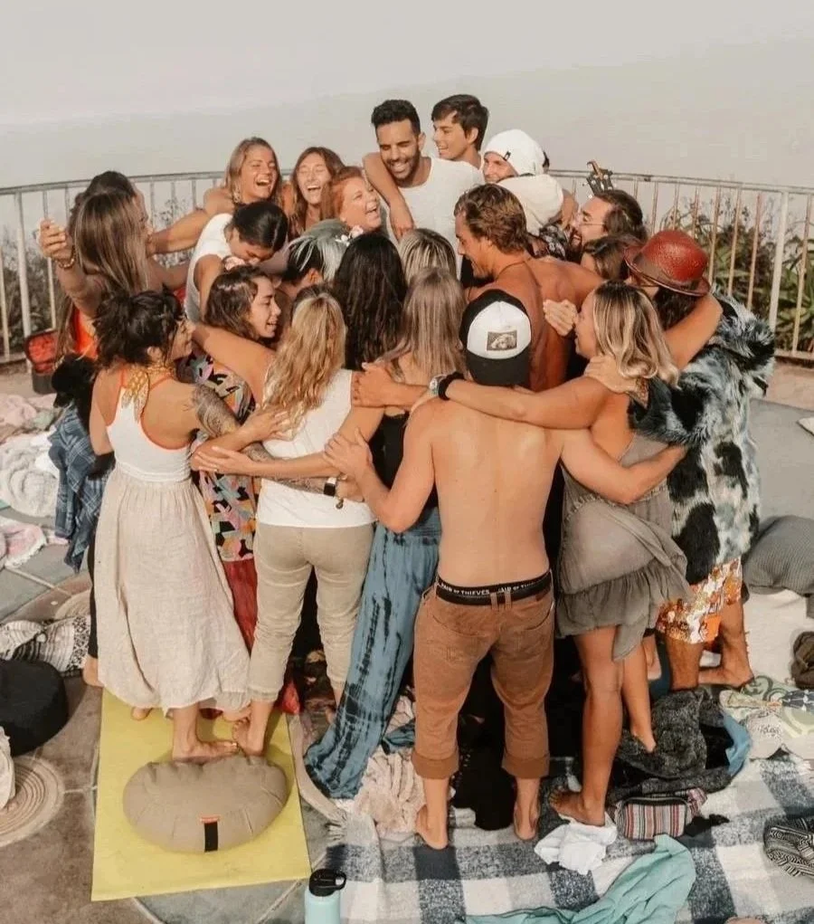 Group of people embracing each other in a circle on a rooftop, celebrating or having a gathering, with some wearing casual summer clothes and hats.