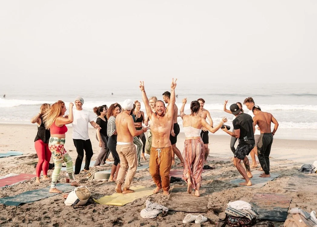 People dancing and celebrating on a beach with ocean waves in the background.
