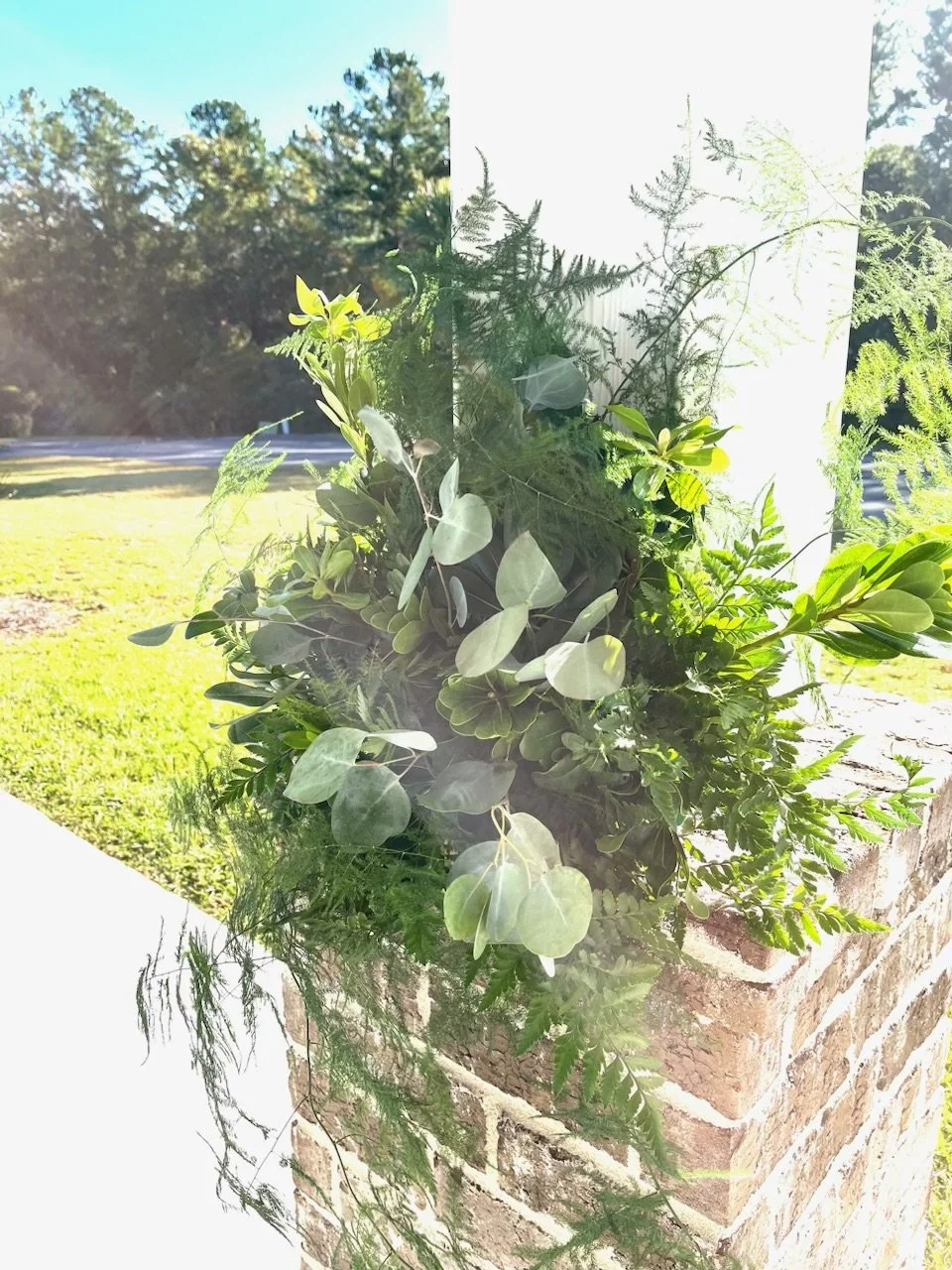 A flower box filled with various green plants and foliage, attached to a brick ledge outside.