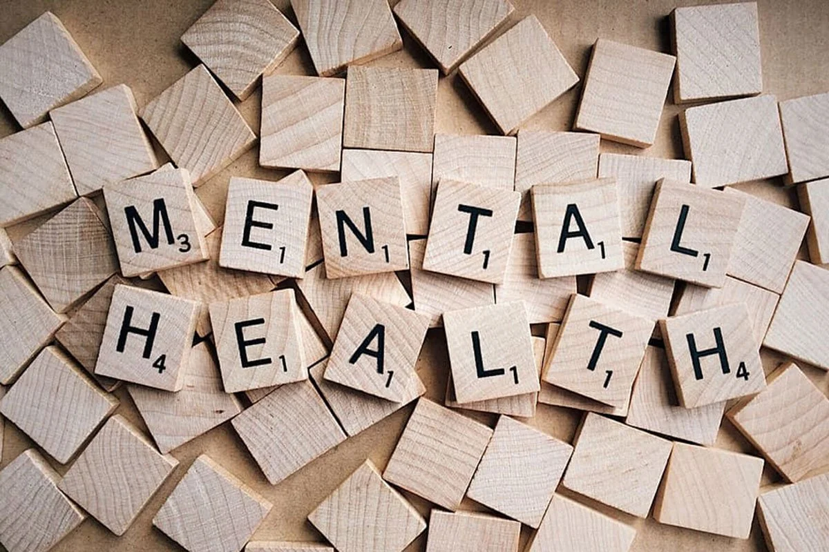 Scrabble tiles arranged to spell out 'MENTAL HEALTH' on a surface with many empty wooden tiles around.