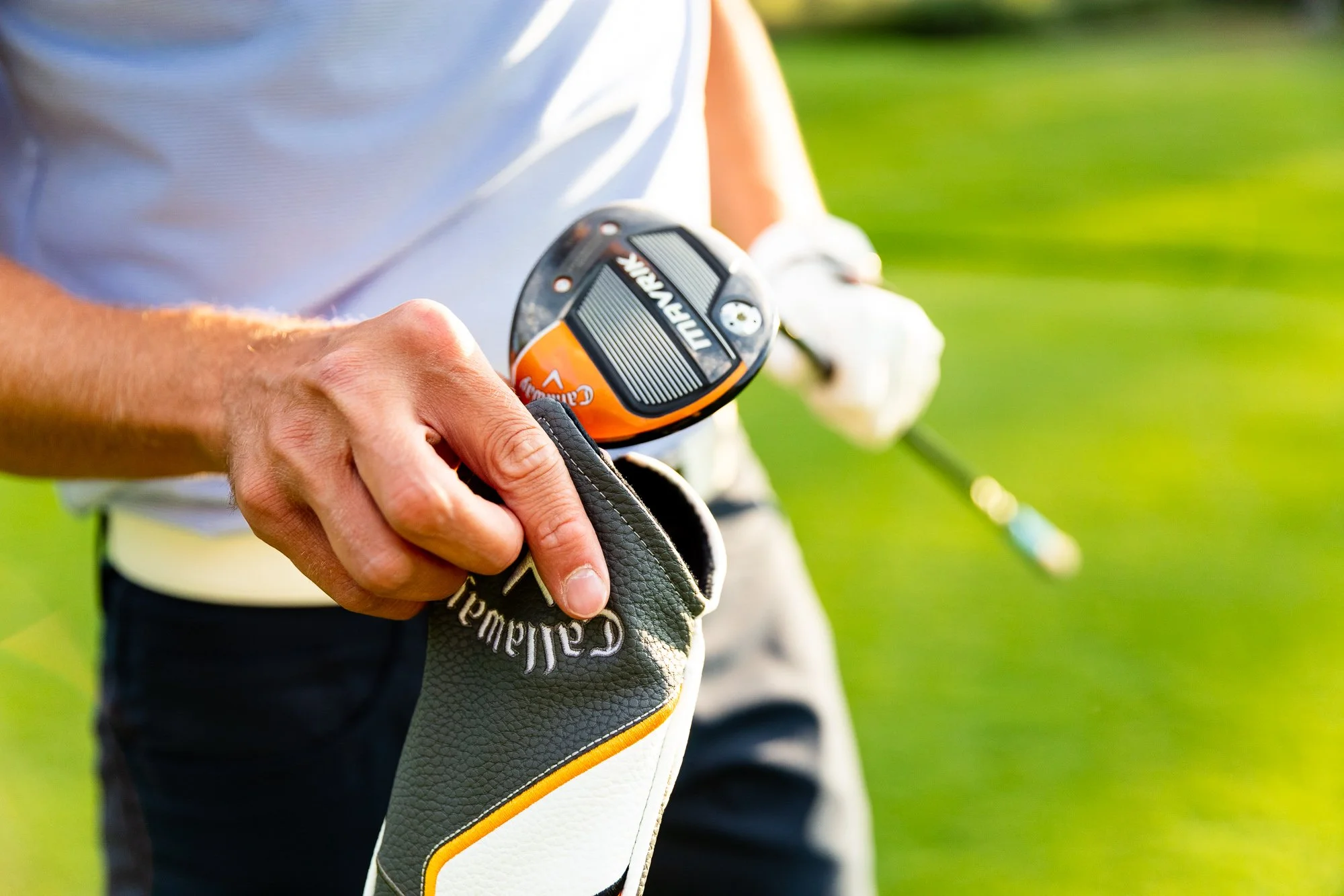 Close-up of a man holding a Callaway golf club and a Garmin golf GPS device on a golf course, with green grass in the background.