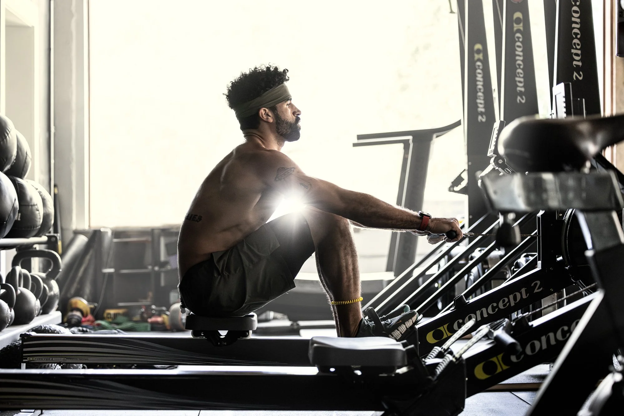 Man with a beard and headband working out on a rowing machine in a gym.