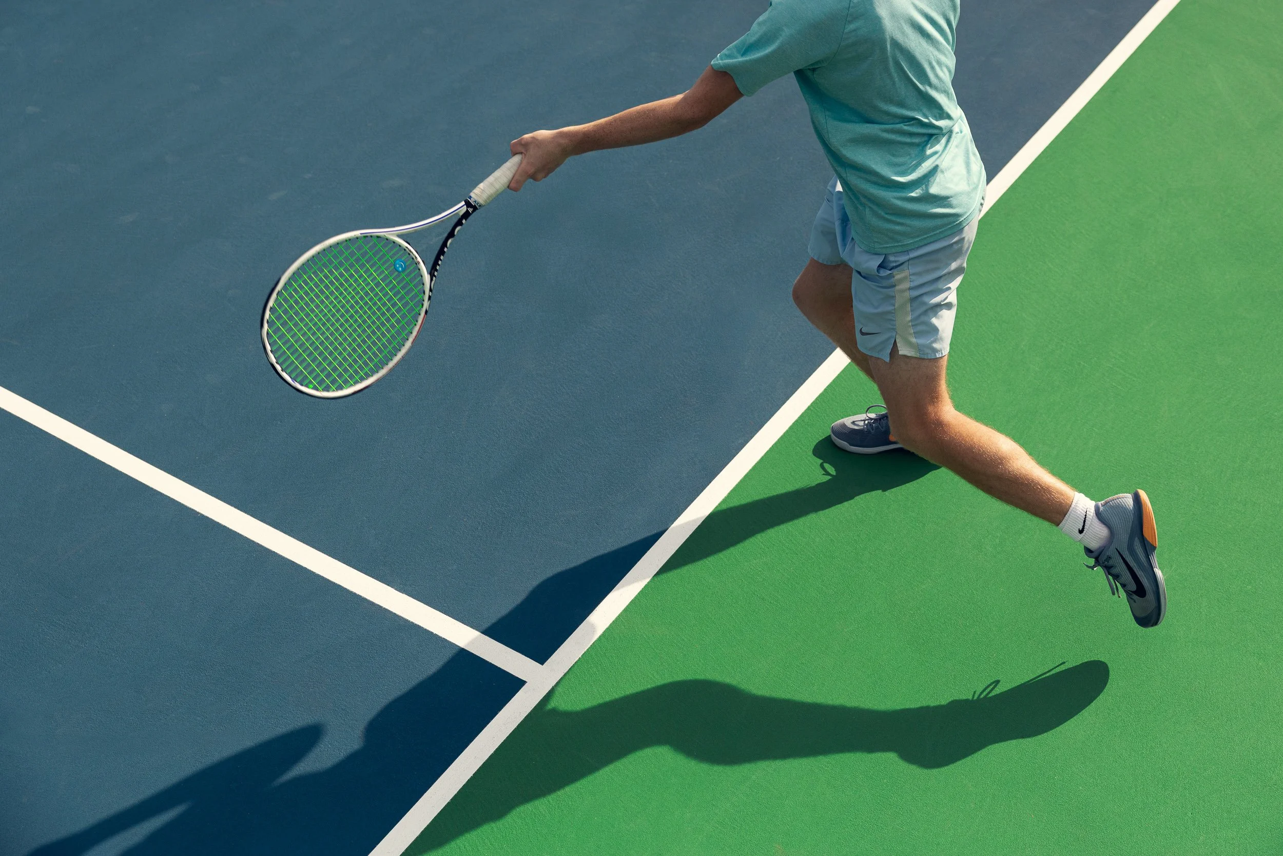 A man playing tennis on a court, reaching to hit a ball with his racket, wearing a turquoise shirt, light blue shorts, and gray shoes.