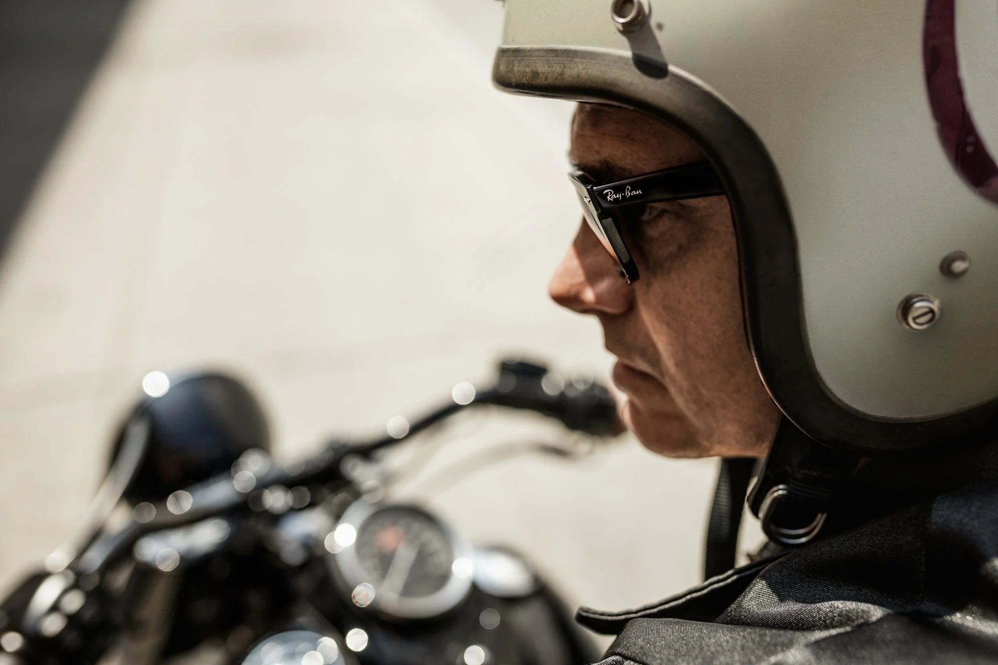 Close-up side profile of a man wearing a motorcycle helmet and sunglasses, sitting on a motorcycle.