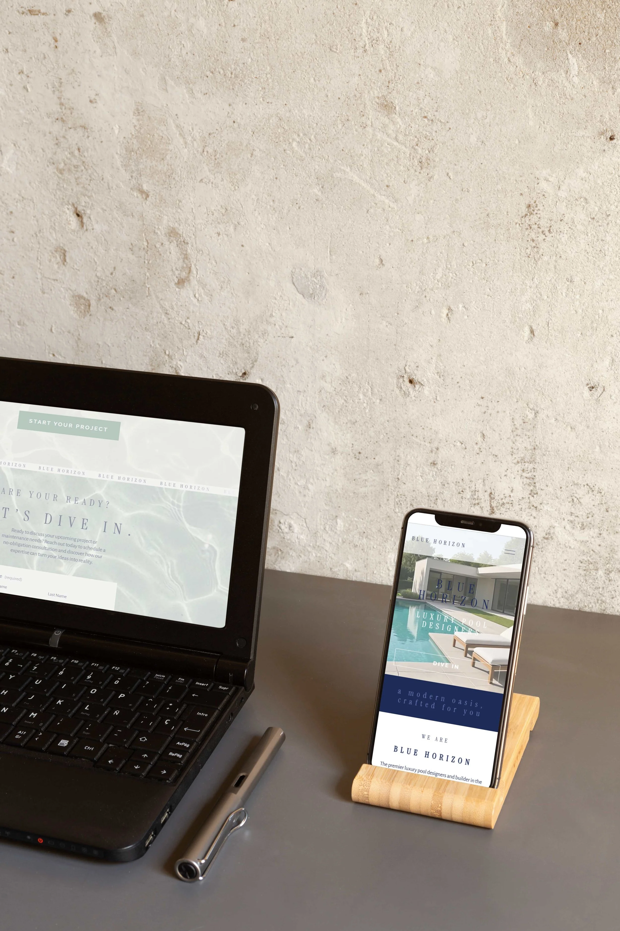 A laptop and an iPhone displaying the Blue Horizon website on a gray desk with a textured wall in the background, a web design case study by Hailey Osborne Designs.
