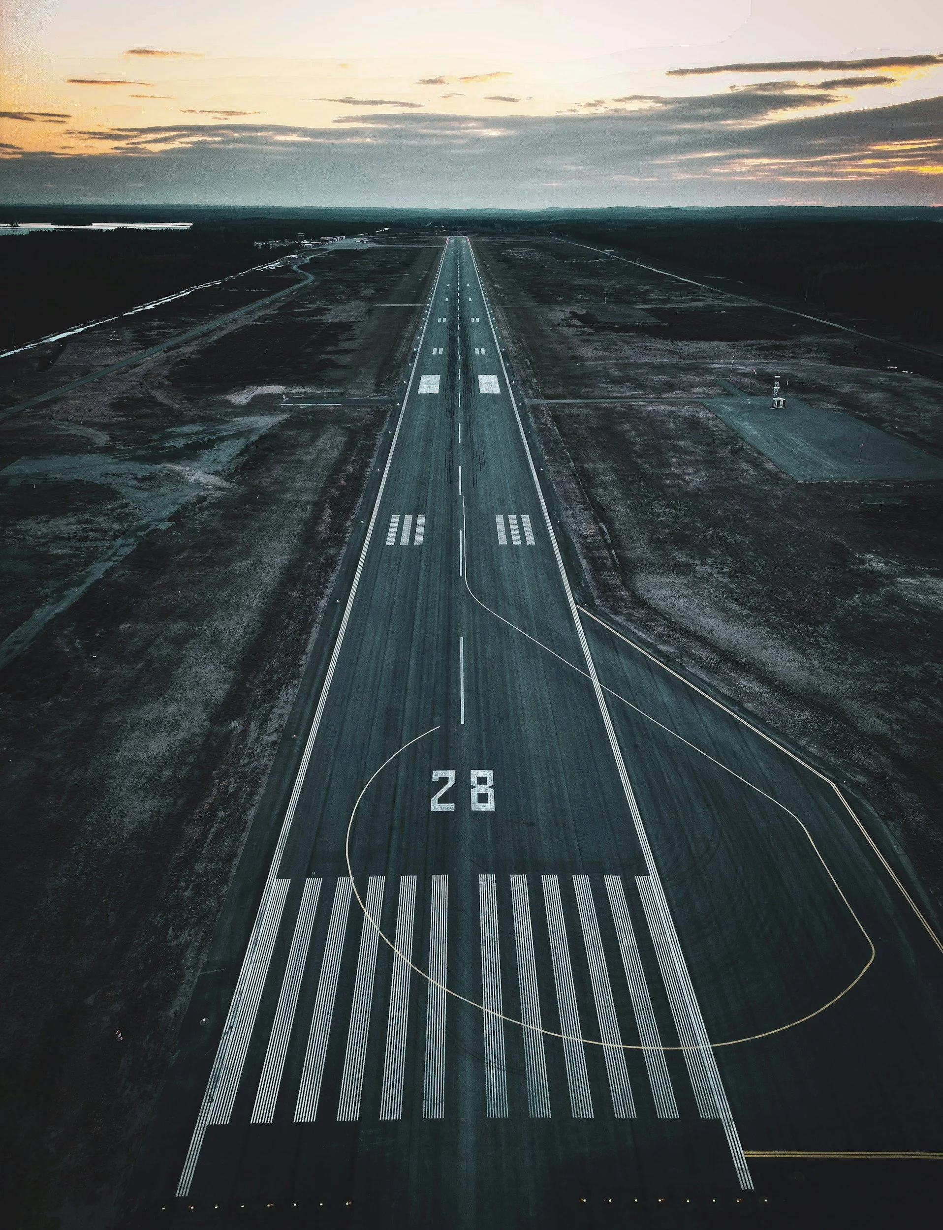 An aerial view of an empty runway at an airport during sunset, with runway markings and the number 28 visible.