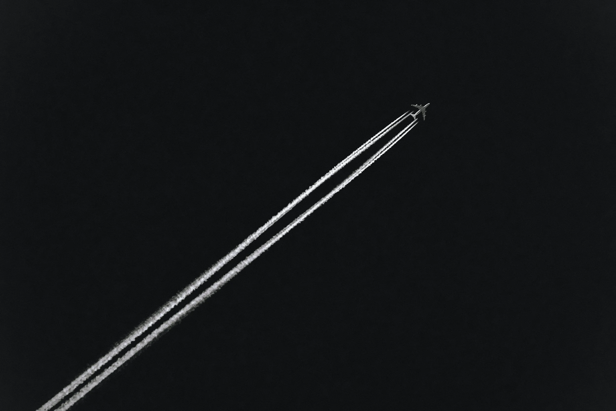 An airplane flying high in the sky, leaving two contrails behind.